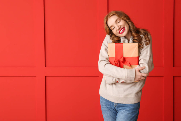 Happy young woman in winter clothes and with Christmas gift on color background - Photo, Image