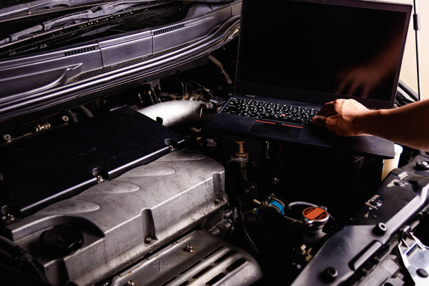 ワークショップでのサービスのための車の整備士のエンジン上のラップトップコンピュータ - 写真・画像