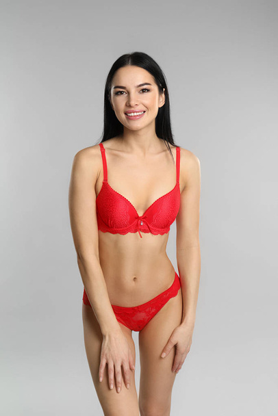 Beautiful young woman in red underwear on grey background - Фото, изображение