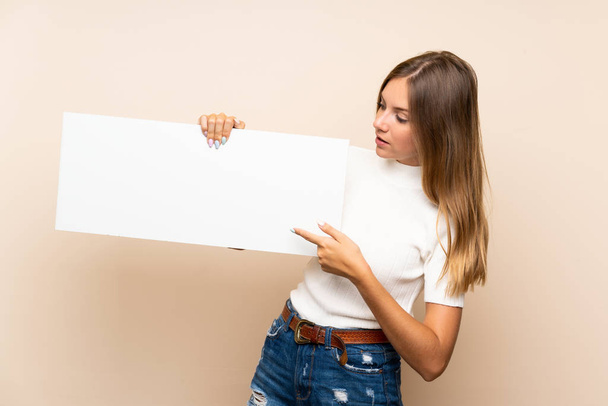Young blonde woman over isolated background holding an empty white placard for insert a concept - Foto, Imagem