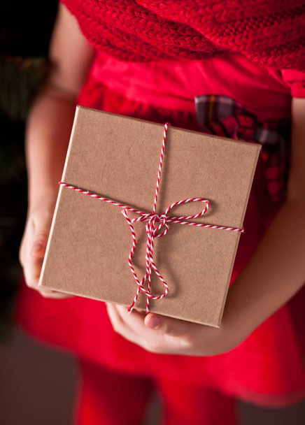 Child girl in red dress holding a Christmas gift box in a hands - Fotografie, Obrázek