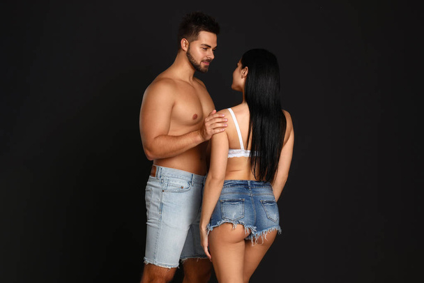 Young woman in underwear and denim shorts with her boyfriend on black background - Photo, Image