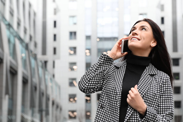 Beautiful woman in stylish suit talking on phone outdoors. Space - 写真・画像
