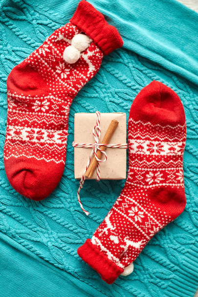 Χριστουγεννιάτικη σύνθεση, κόκκινες κάλτσες με δώρο σε μπλε πλεκτό πουλόβερ με γιρλάντα και κώνους - Φωτογραφία, εικόνα