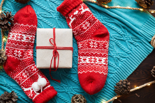 Composición navideña, calcetines rojos con un regalo en un suéter de punto azul con una guirnalda y conos
 - Foto, imagen