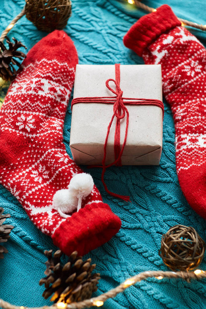 Рождественская композиция, красные носки с подарком на голубом трикотажном свитере с гирляндой и конусами
 - Фото, изображение