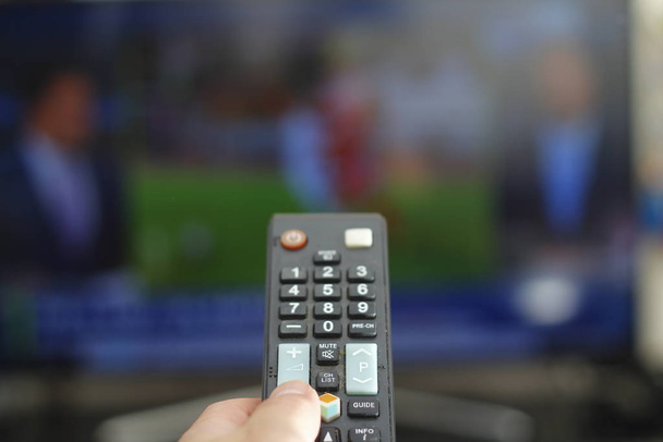 Una persona con un control remoto de TV controla el control remoto para cambiar los canales para ver programas de televisión
. - Foto, imagen
