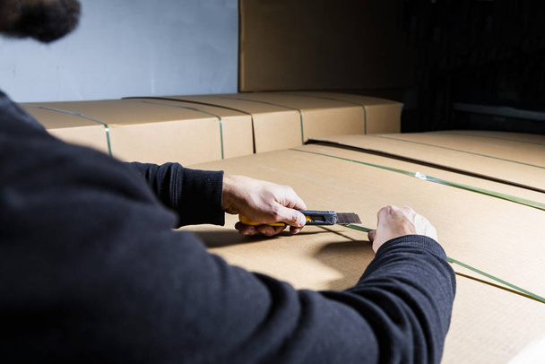 Man using an utility knife to open a cardboard box. Opening packages in a warehouse. Unboxing. - Фото, изображение
