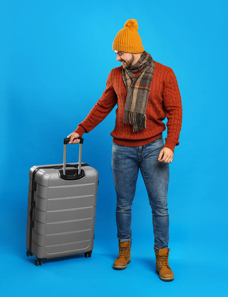 Young man in warm clothes with suitcase on blue background. Winter vacation - Photo, Image