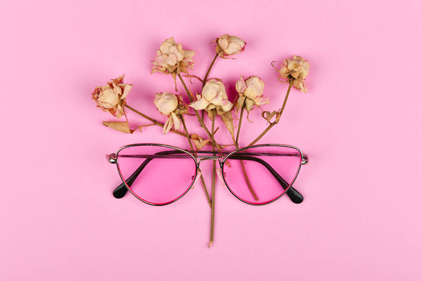 pink glasses in colors. flat lay. Glamor and style. Glasses for women. Pink glasses on a pink background decorated with dried roses. - Foto, imagen