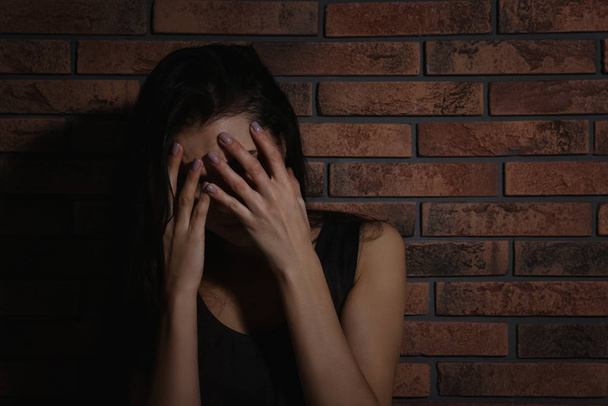 Crying young woman near brick wall. Domestic violence concept - Foto, afbeelding