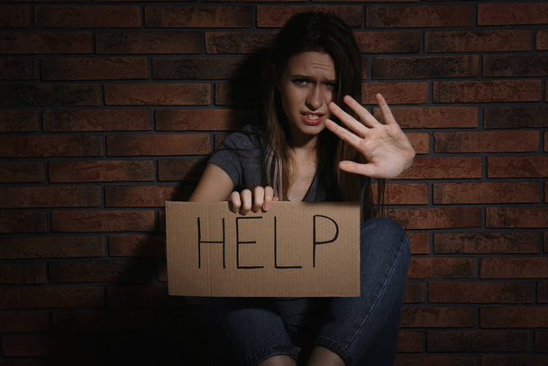 Abused young woman with sign HELP making stop gesture near brick wall. Domestic violence concept - Foto, Imagem