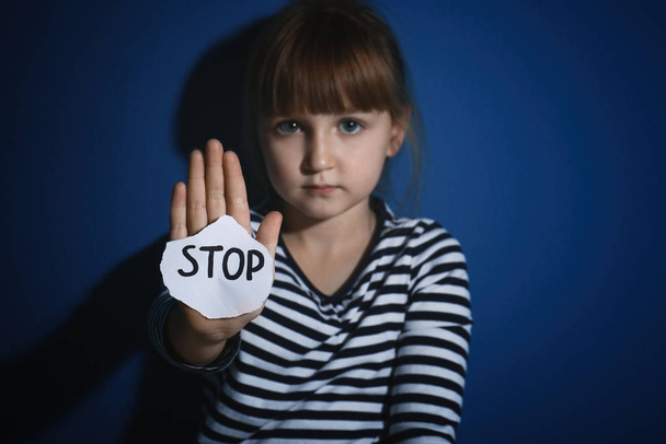 Abused little girl with sign STOP near blue wall, focus on hand. - Photo, image