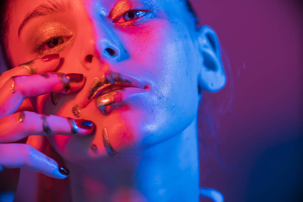 Modelo de moda lábios de prata metálica e mulher rosto em luzes azuis e roxas neon uv, posando em estúdio, menina bonita, maquiagem brilhante, maquiagem colorida
 - Foto, Imagem