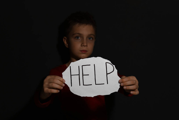 Abused little boy with sign HELP near black wall. Domestic viole - Fotoğraf, Görsel