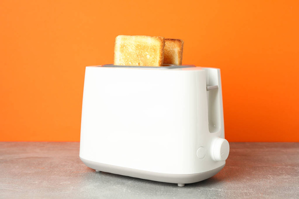 Toaster with bread on grey table against orange background, clos - Photo, Image