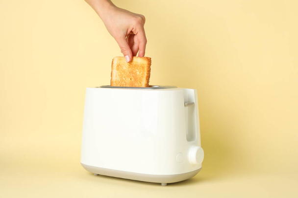 Female hand puts bread in a toaster on beige background, space f - Photo, Image