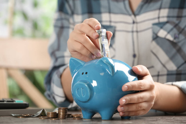 Woman putting money into piggy bank at table, closeup - Photo, Image