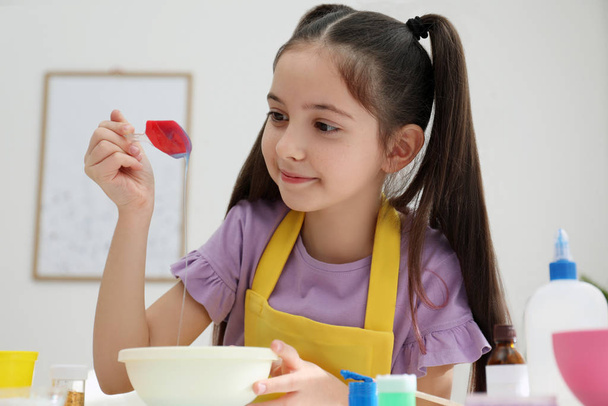 Cute little girl mixing ingredients with silicone spatula at table in room. DIY slime toy - Foto, afbeelding