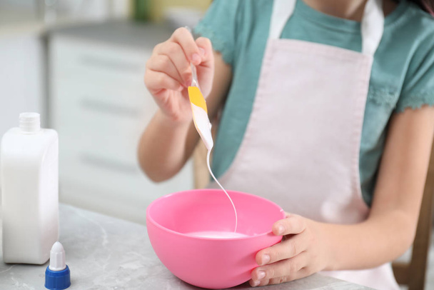 Little girl mixing ingredients with silicone spatula at table in kitchen, closeup. DIY slime toy - Φωτογραφία, εικόνα