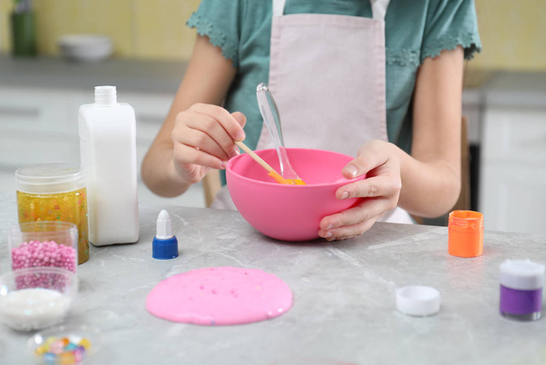 Little girl making homemade slime toy at table in kitchen, closeup - Фото, изображение