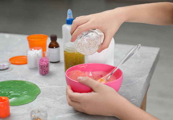 Little girl adding sparkles into homemade slime toy at table, closeup of hands - Photo, image