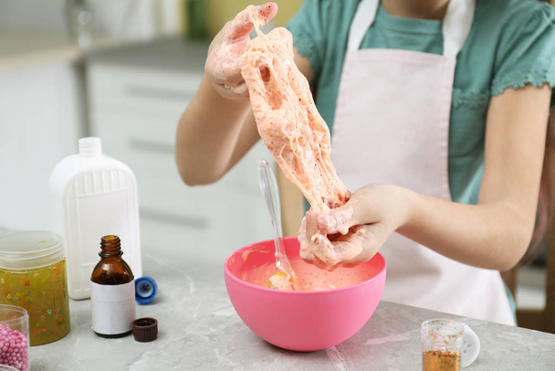 Little girl kneading DIY slime toy at table in kitchen, closeup - Foto, imagen
