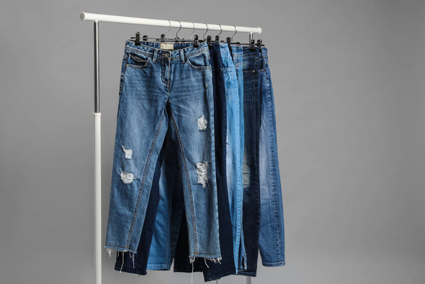 Rack with different jeans on grey background - 写真・画像