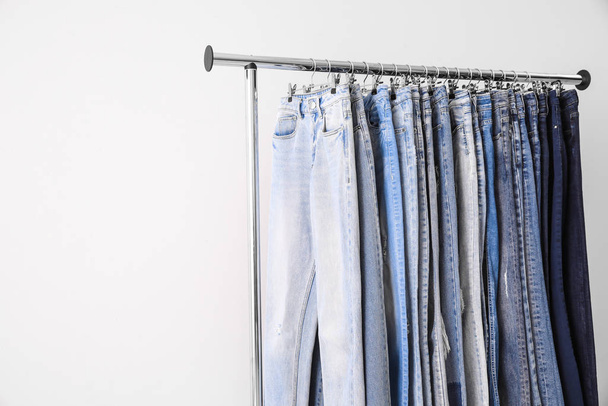 Rack with different jeans on light background. Space for text - Φωτογραφία, εικόνα