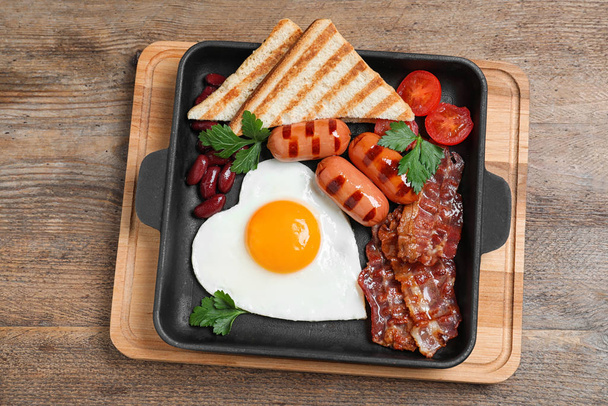 Delicious breakfast with heart shaped fried egg and  sausages on wooden table, top view - Фото, зображення