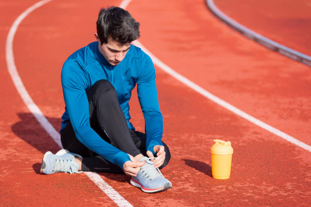Close up view, of an athlete tying his shoe laces. Man tightening his shoe laces sitting on the ground on a running track. - Foto, Imagem
