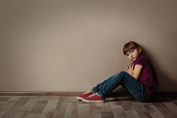 Sad little girl sitting on floor indoors, space for text. Child  - Фото, изображение
