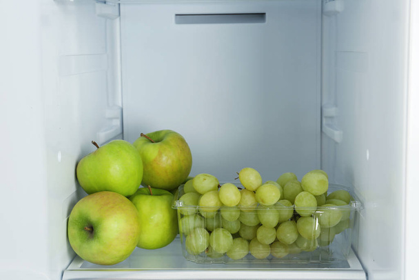 Apples and grapes on shelf in refrigerator - Фото, зображення