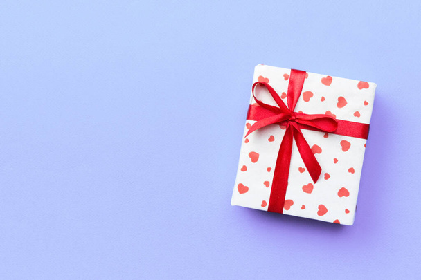Caja de regalo con cinta roja y corazón sobre fondo púrpura, vista superior con espacio de copia para texto
 - Foto, imagen