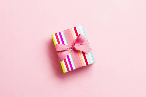 wrapped Christmas or other holiday handmade present in paper with pink ribbon on pink background. Present box, decoration of gift on colored table, top view with copy space - Photo, Image