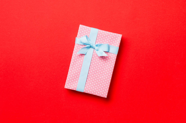 verpackte Weihnachten oder andere Feiertage handgemachtes Geschenk in Papier mit blauem Band auf rotem Hintergrund. Geschenkschachtel, Geschenkdekoration auf farbigem Tisch, Draufsicht mit Kopierraum - Foto, Bild