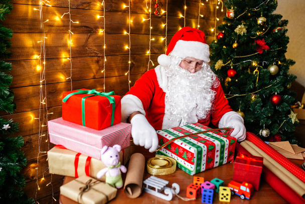 Merry Christmas and Happy Holidays. Santa Clause is preparing gifts for children for Xmas at desk at home. - Foto, Imagem