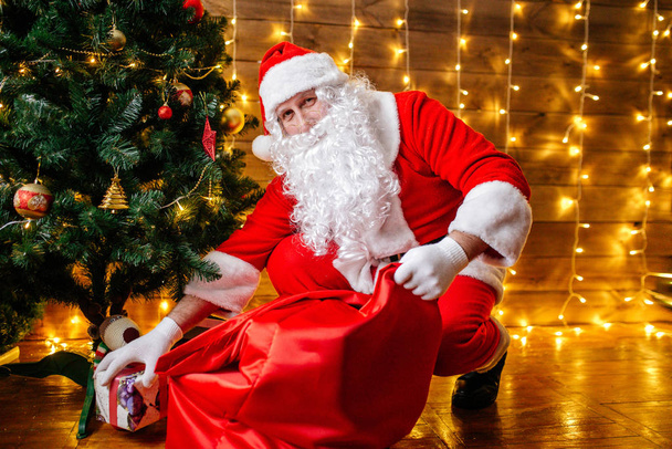 Santa Claus poblíž vánoční stromeček s dárky. Vánoční čas - Fotografie, Obrázek