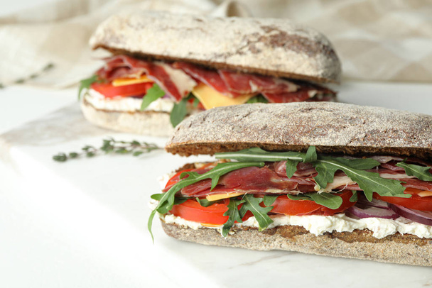 Delicious sandwiches with fresh vegetables and prosciutto on white table, closeup - Фото, зображення