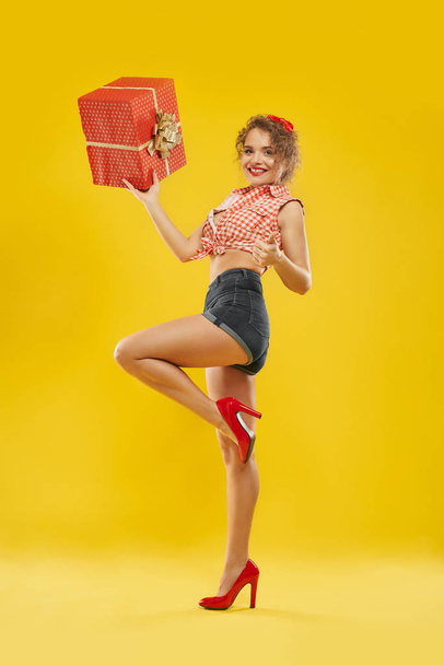 Lady standing on one leg holding red box with golden bow. - Фото, изображение