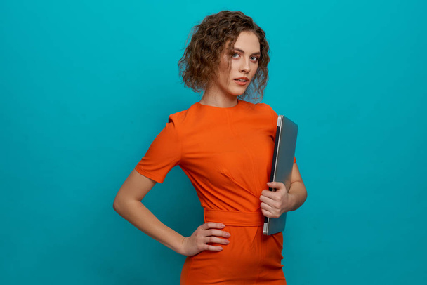Slender woman in orange dress holding laptop. - Foto, afbeelding