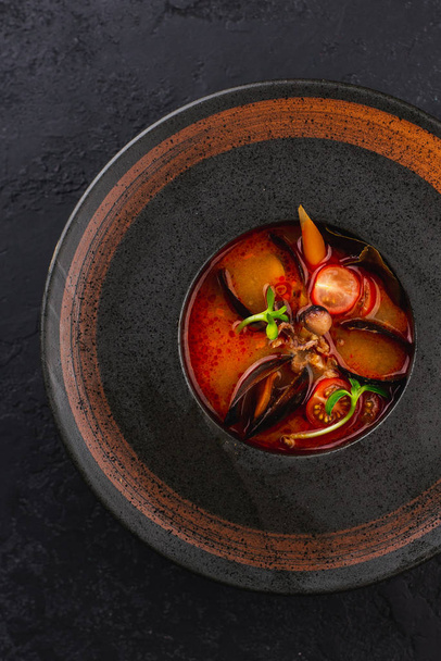 red tomato soup with mussels and vegetables on black plate - Foto, Imagen