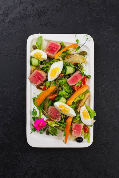 зелений салат з вареними яйцями і шматочками тунця на білій тарілці
 - Фото, зображення