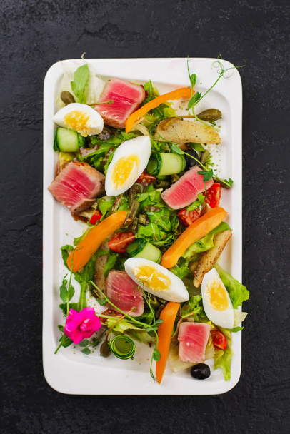 zielona sałatka z gotowanymi jajami i kawałkami steku z tuńczyka na białym talerzu - Zdjęcie, obraz