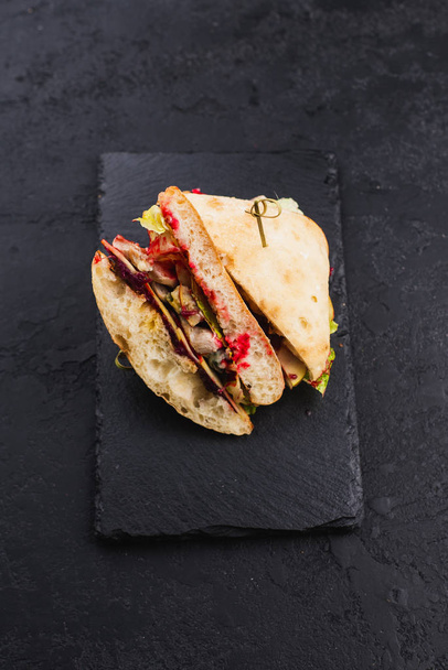 ciabatta valkoinen leipä voileipiä kanaa, salaatteja ja juustoja mustalla lautasella
 - Valokuva, kuva