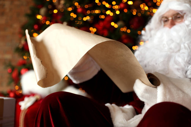 Santa Claus reading wish list against blurred festive lights, closeup - Φωτογραφία, εικόνα