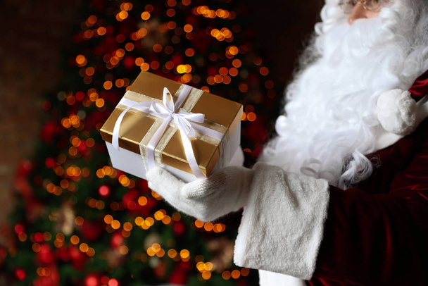 Santa Claus holding Christmas gift against blurred festive lights, closeup - Фото, зображення