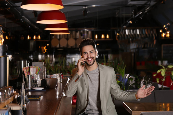Young business owner talking on phone in his cafe - Photo, image