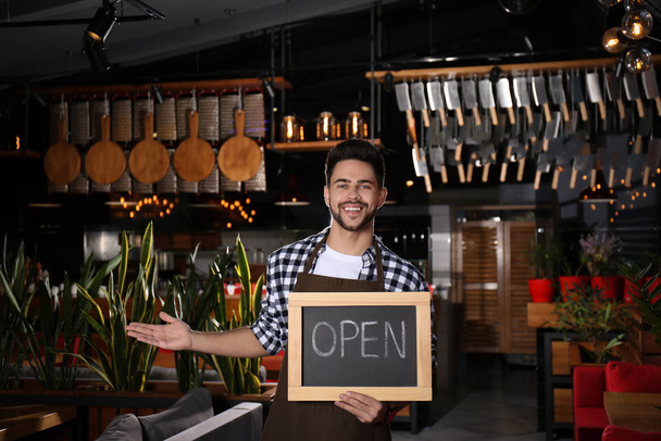 Young business owner holding sign OPEN in his cafe - Foto, immagini