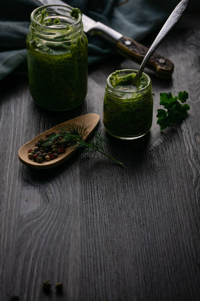 Green pesto sauce in glass jars with pepper and parsley  - Фото, зображення
